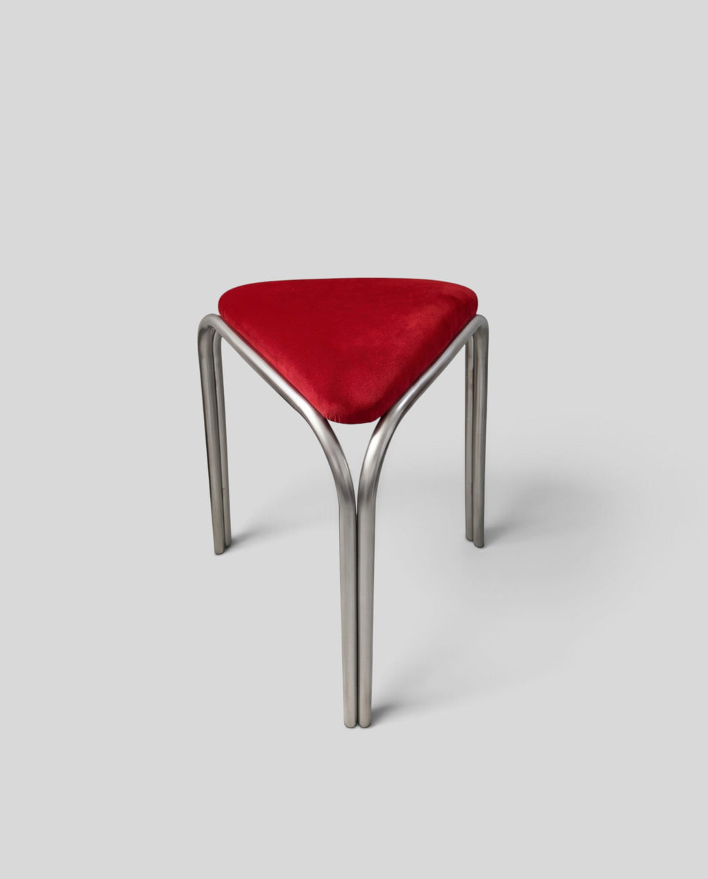 ESTYNE Studio Atelier stool with a triangular red velvet seat and a polished stainless steel frame on a marble floor.