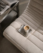ESTYNE Studio Form Cup in off-white ceramic resting on a small metal tray atop a textured cream armchair