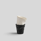 ESTYNE Studio Form Cup set featuring one off-white and one black hand-formed ceramic cup stacked on a light grey background.